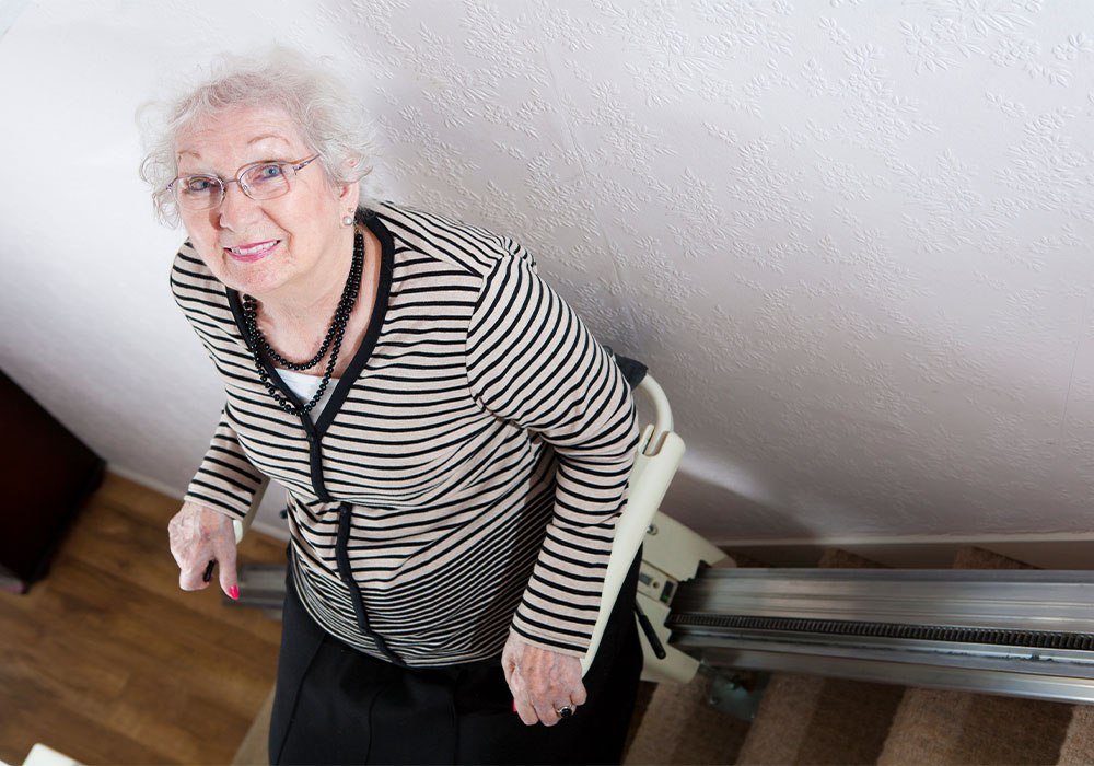 elderly woman riding up stairlift in home